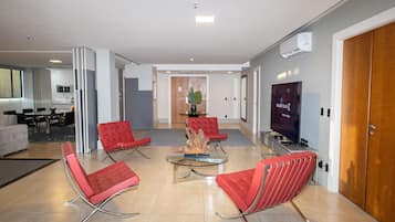 A modern hotel lobby with red chairs, a glass coffee table, a flat-screen TV, and a wooden door.