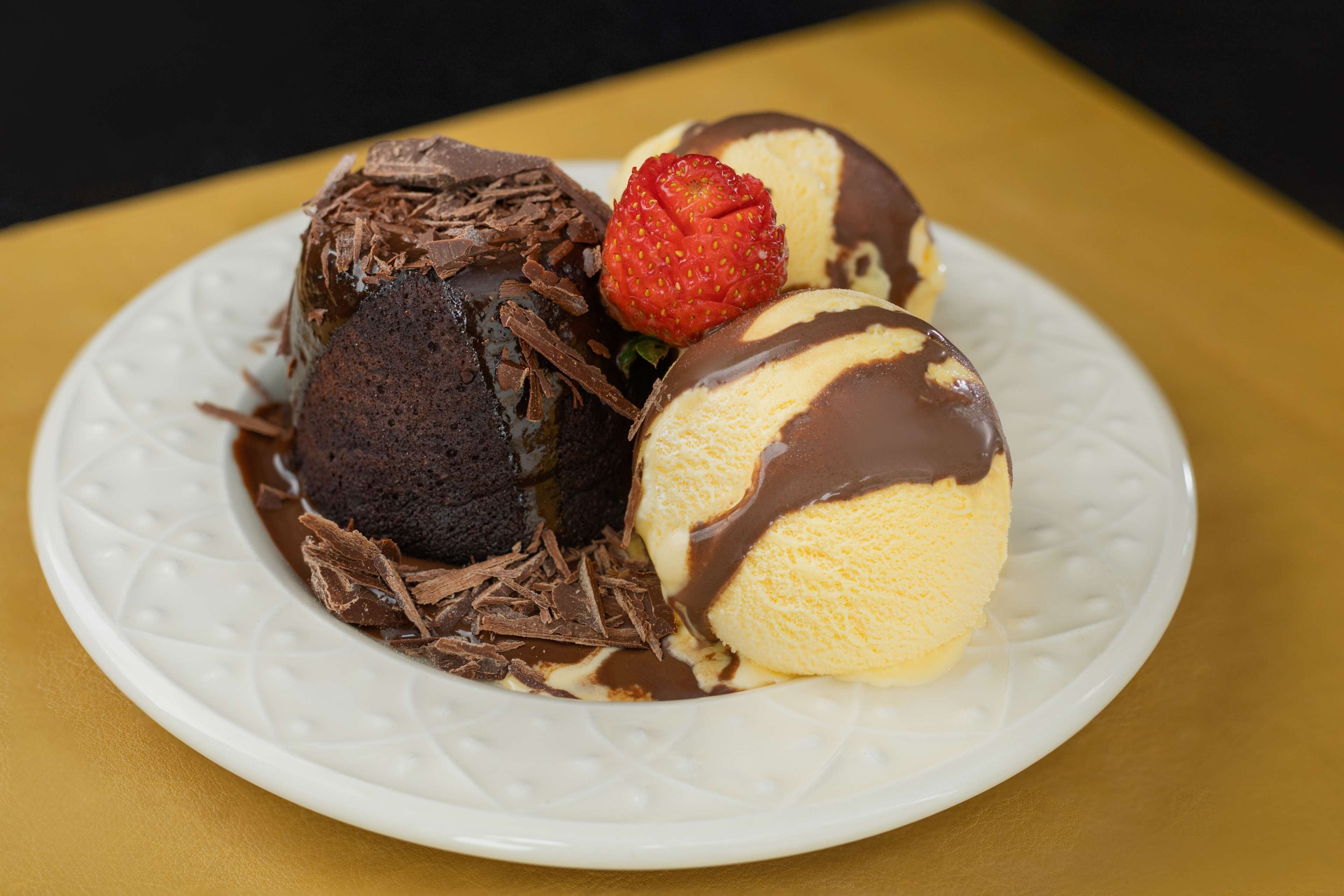 Un plato de postre con pastel volcán de chocolate, helado de vainilla y una fresa.