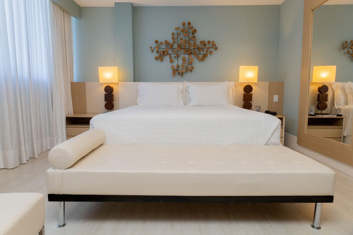A modern hotel room with a large bed, two bedside tables, and a wall-mounted lamp.
