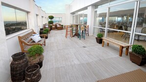 A rooftop terrace with seating, potted plants, and a view of the city. - Golden Tulip Porto Vitória (Vitoria)