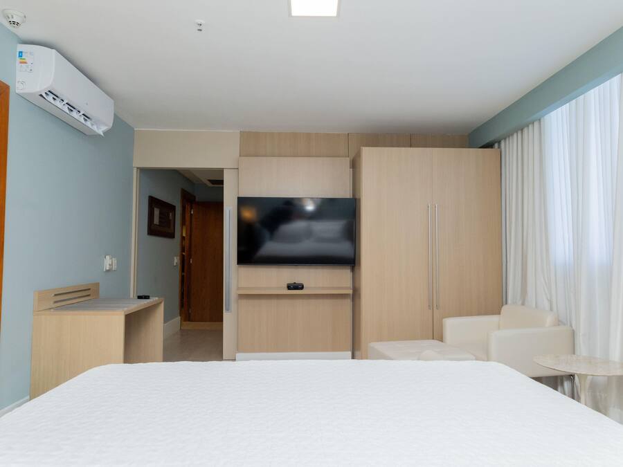 A hotel room with a bed, a TV mounted on the wall, a desk, a chair, and a small table.