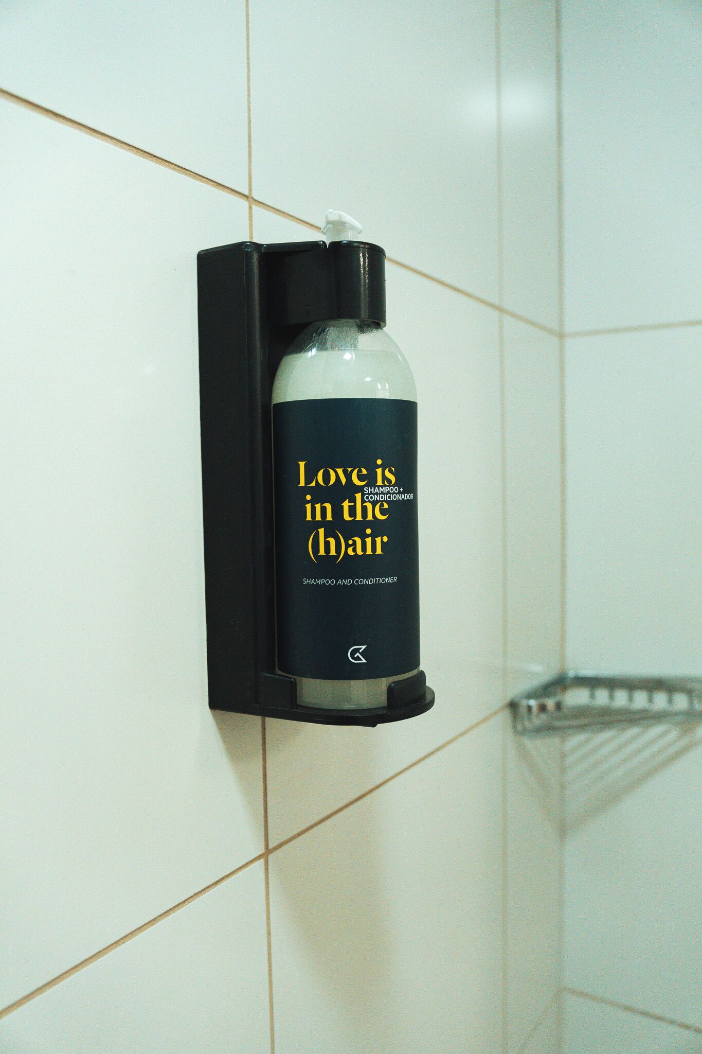 A bottle of shampoo and conditioner mounted on a tiled wall.