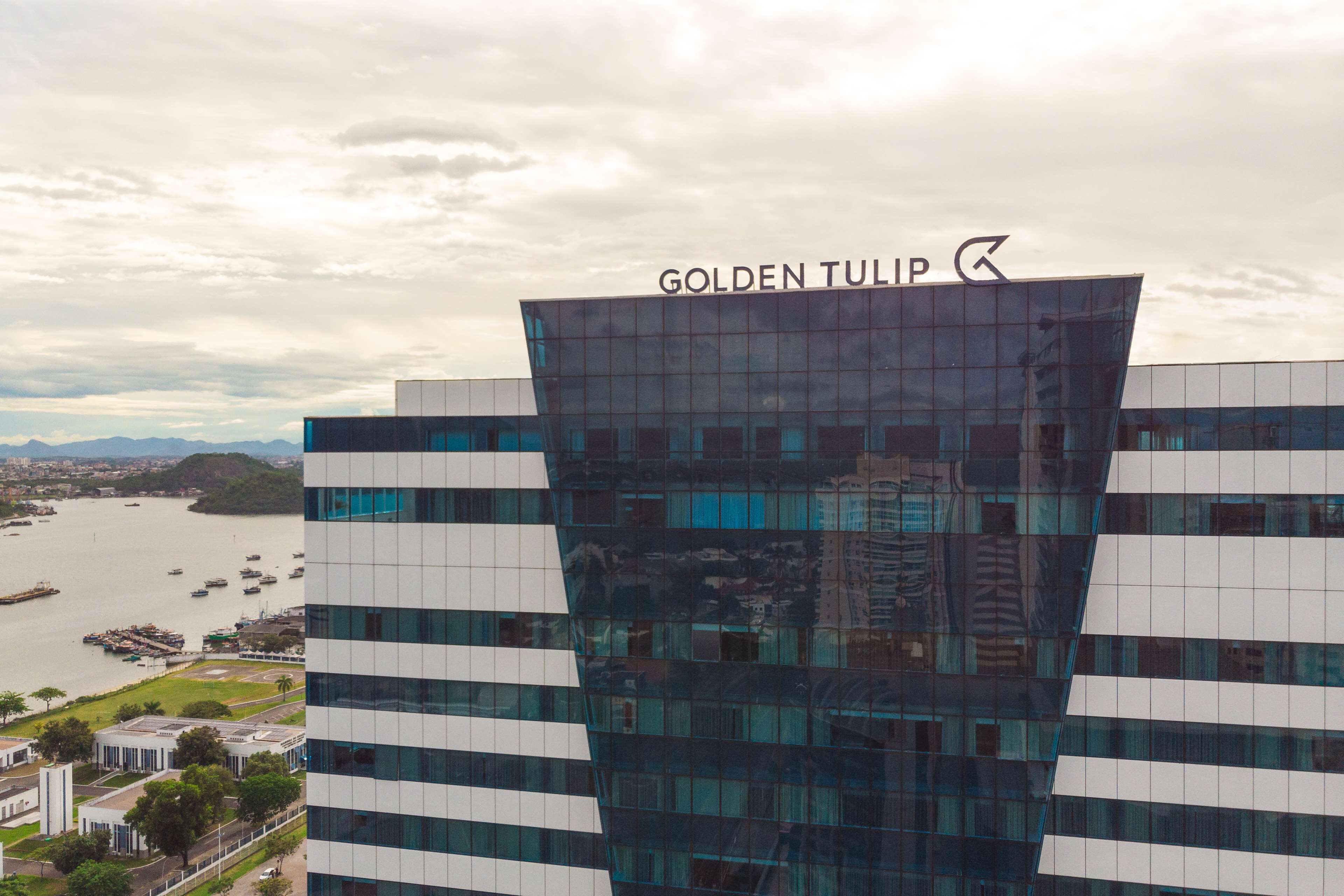 Een modern gebouw met het bord "Golden Tulip" erop, met een uniek hoekig ontwerp en grote ramen die het omliggende stadsbeeld weerspiegelen.
