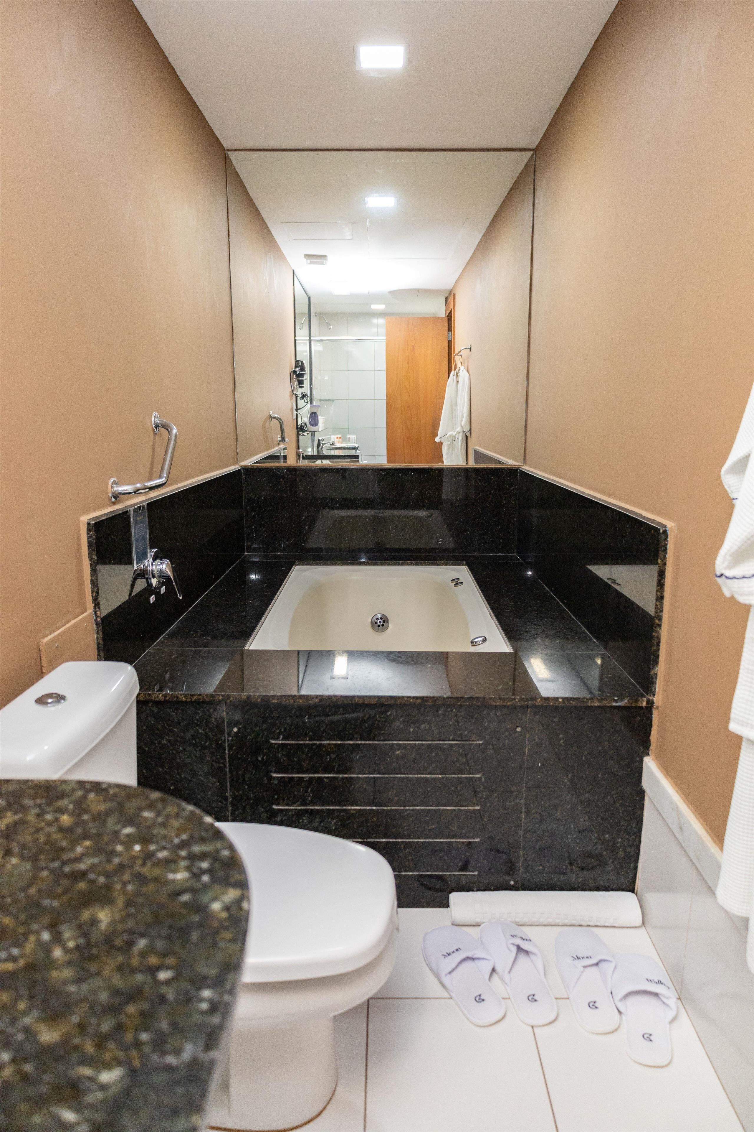 Un baño moderno con un lavamanos de mármol negro, un inodoro blanco y una bañera.