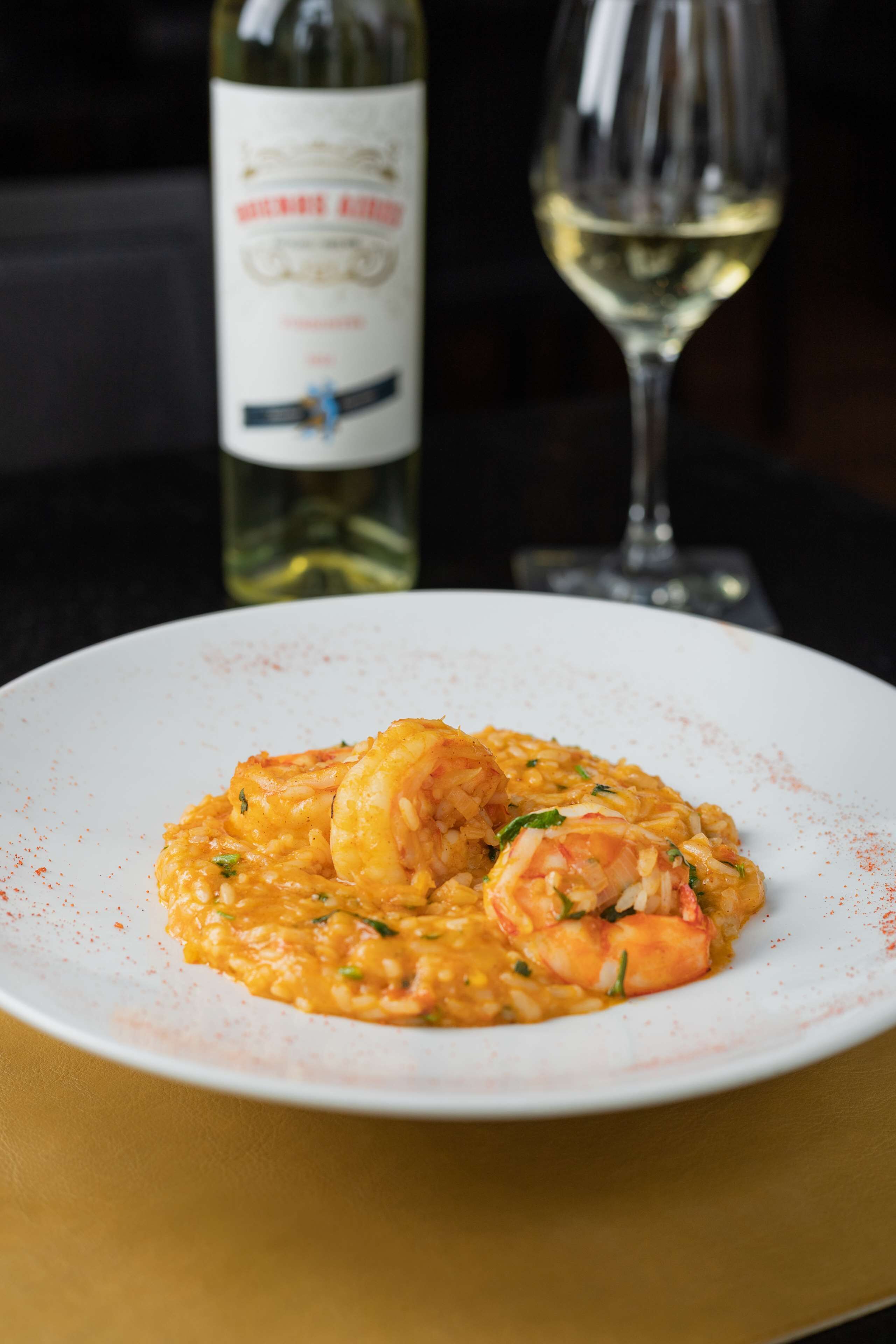 A plate of shrimp risotto with a bottle of wine and a glass in the background.