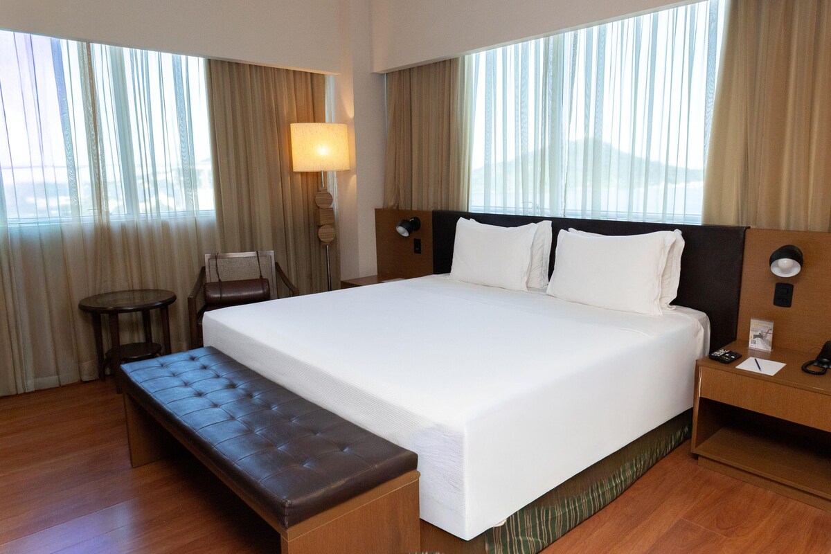A hotel room with a large bed, a bedside table, a lamp, and a bench.