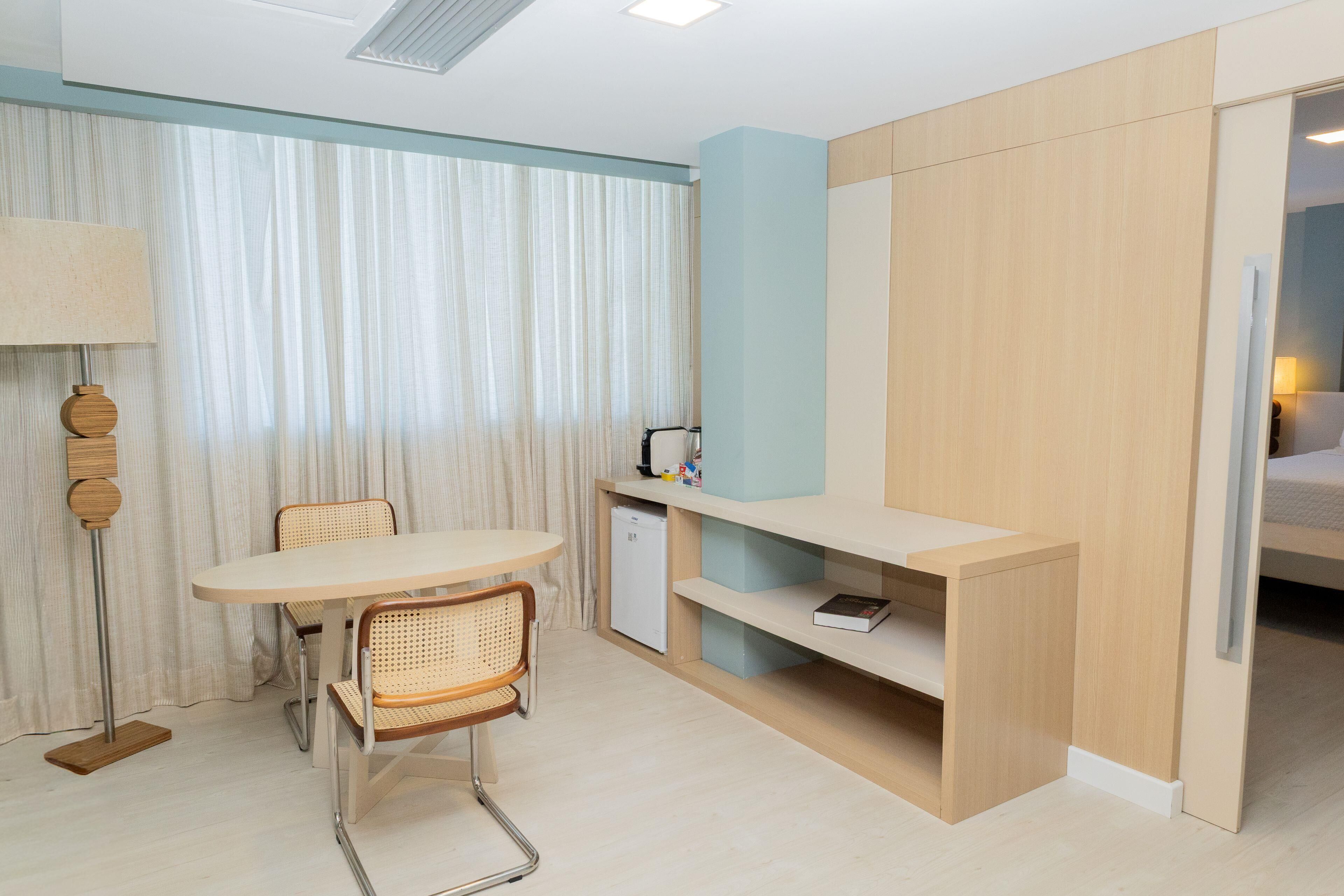 A compact hotel room with a dining table, chairs, a small kitchenette, and a wardrobe.