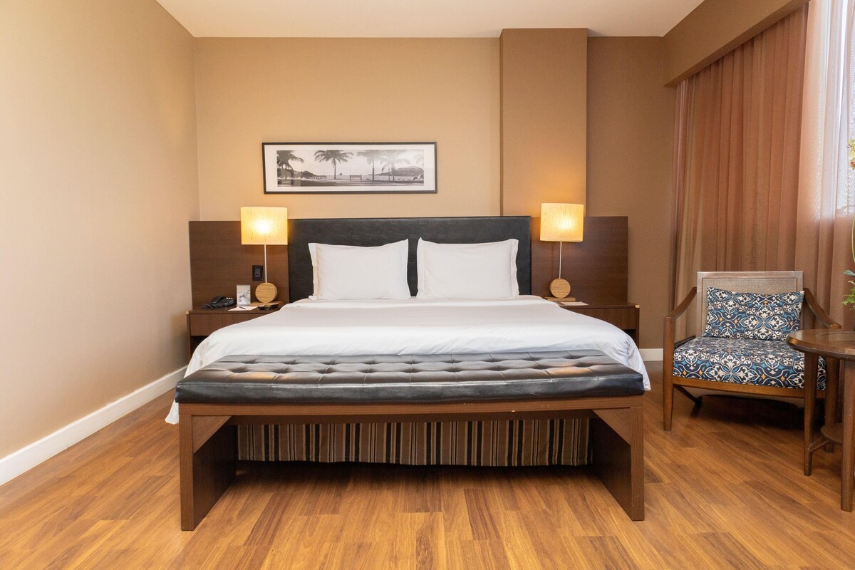 A hotel room with a large bed, two bedside tables, a chair, and a framed picture on the wall.