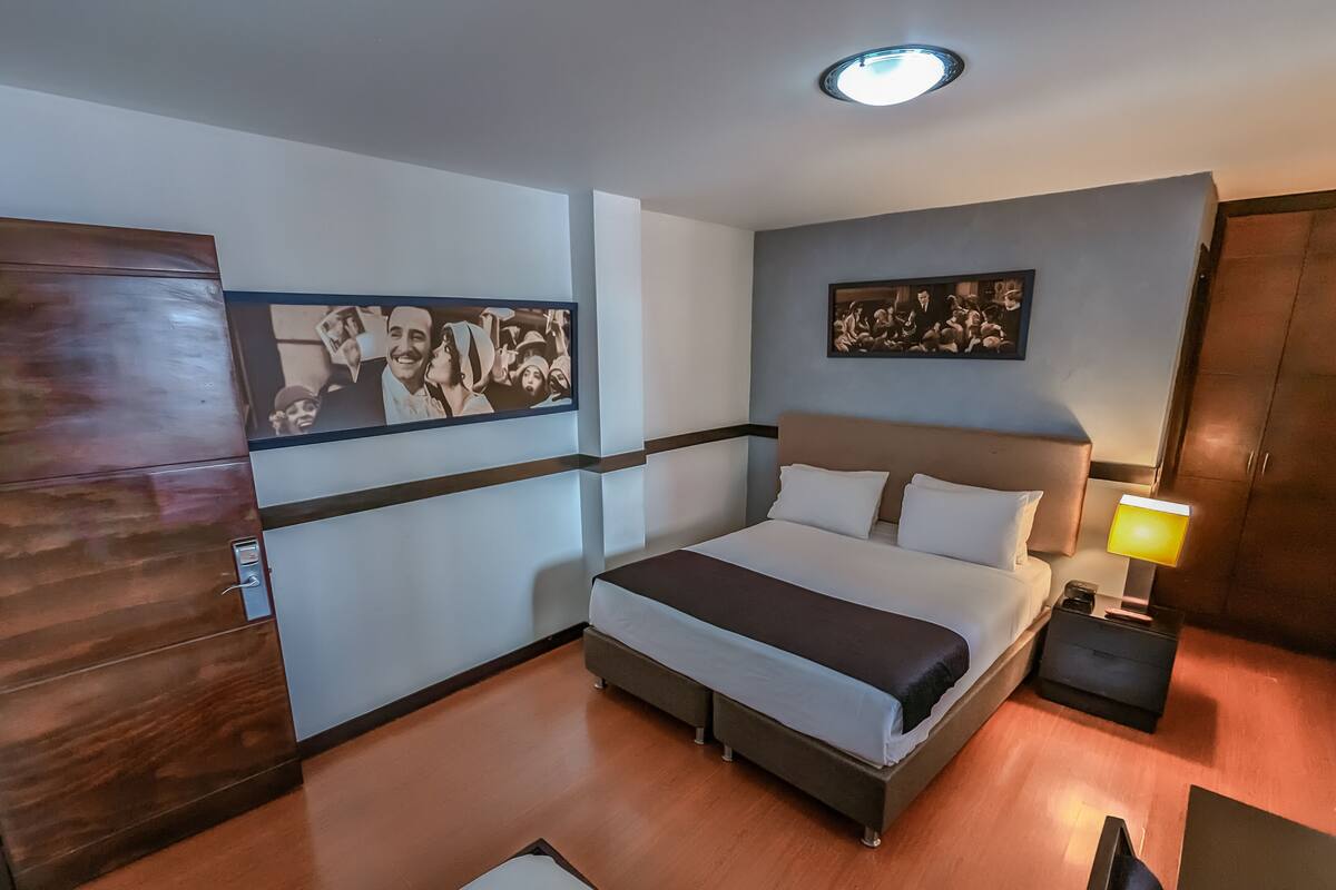 Una habitación de hotel con una cama, mesitas de noche, una lámpara y un armario.