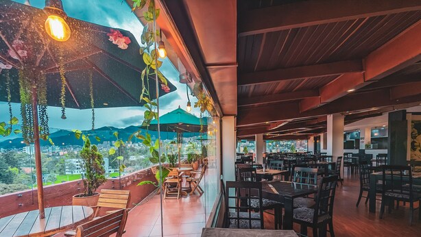 An outdoor dining area with wooden tables and chairs, potted plants, and hanging lights. - Hotel Charlotte Suite 26 (Bogotá)