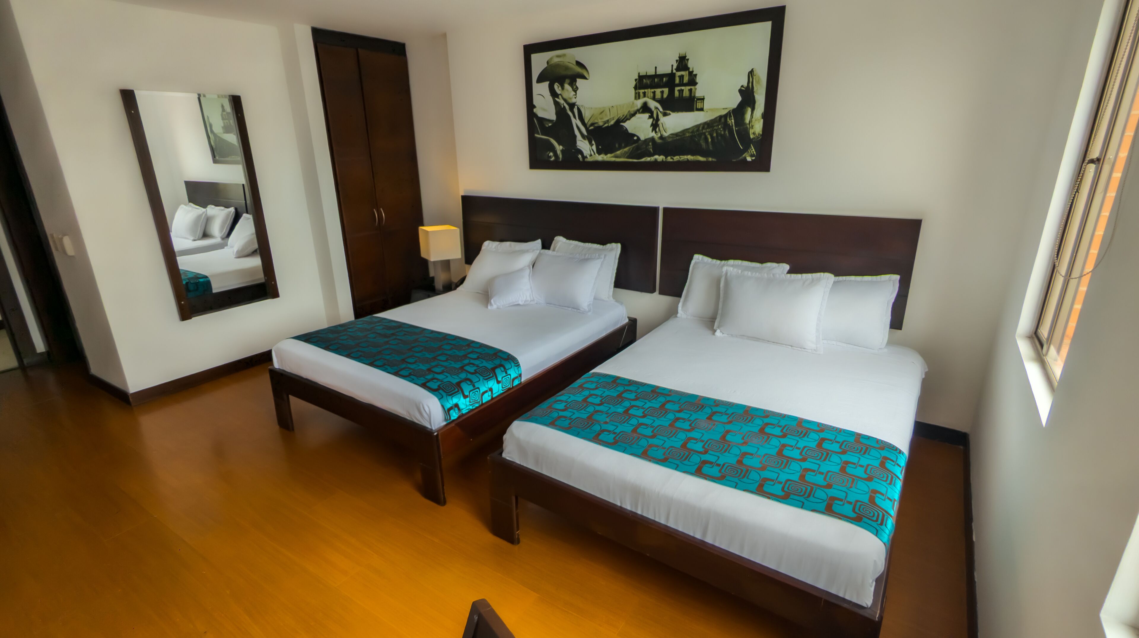 Habitación de hotel con dos camas, un espejo grande, un armario y un cuadro en la pared.