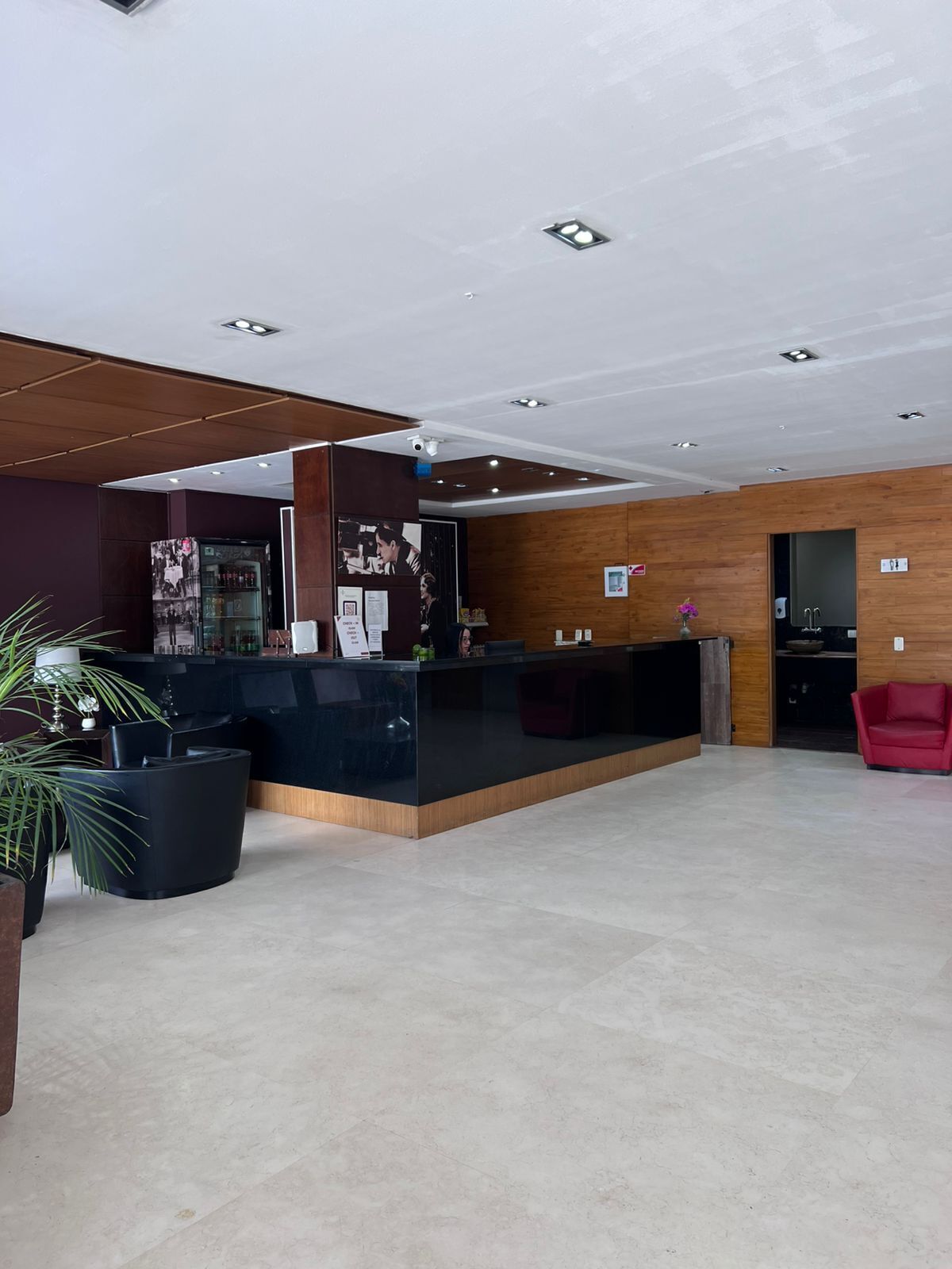 A modern reception area with a dark reception desk, wooden panel walls, and a red chair.
