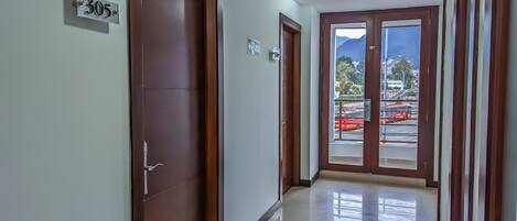 Un pasillo con puertas de madera, un cartel con número y vista a una calle con vehículos.