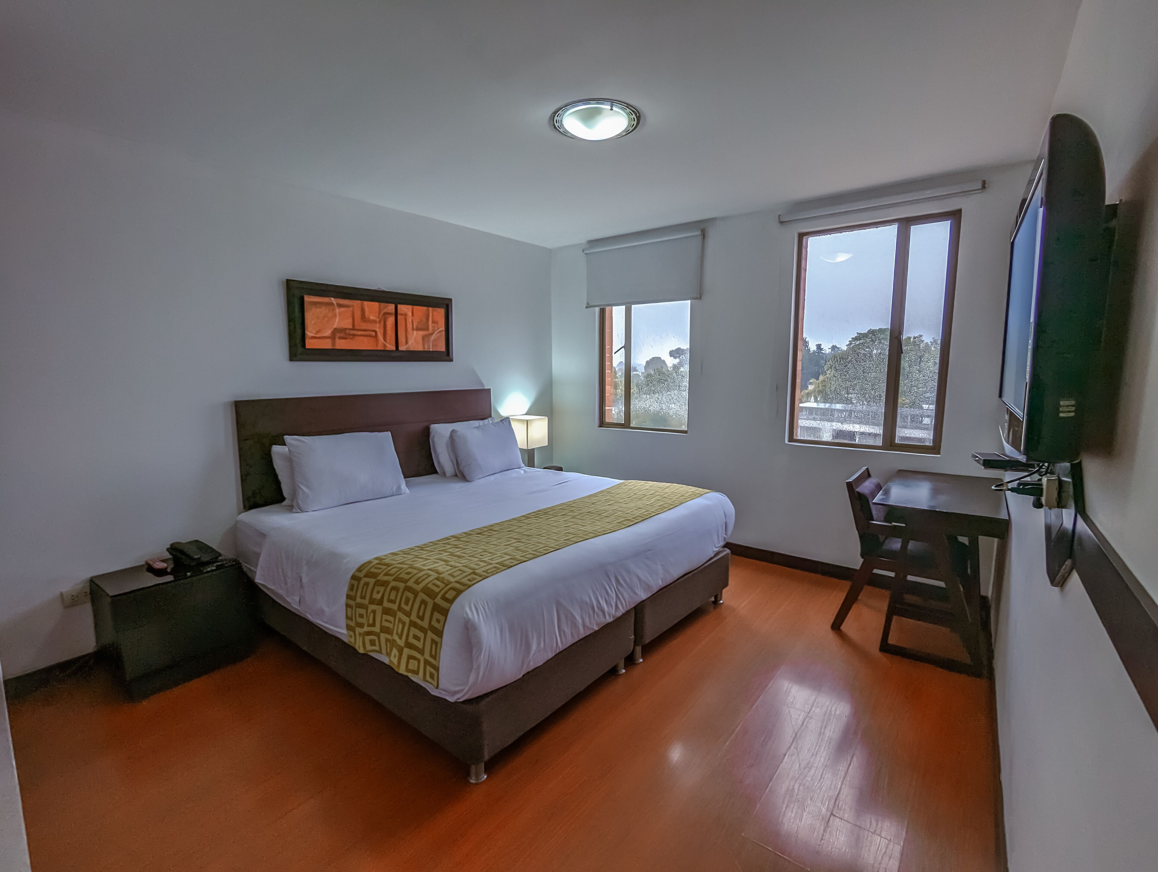 Ein Hotelzimmer mit Bett, Nachttisch, Lampe und einem an der Wand befestigten Fernseher.