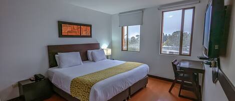 Ein Hotelzimmer mit Bett, Nachttisch, Lampe und einem an der Wand befestigten Fernseher.
