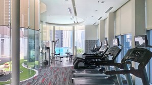 A modern gym with treadmills, weight machines, and a view of a cityscape through large windows. - Somerset Kuala Lumpur (Kuala Lumpur)