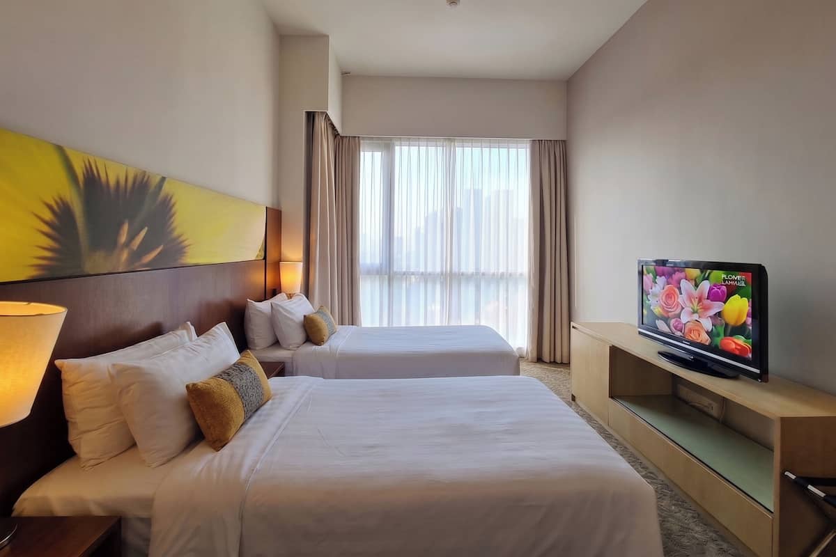 Habitació d'hotel amb dos llits, televisió, un quadre i una finestra amb cortines.