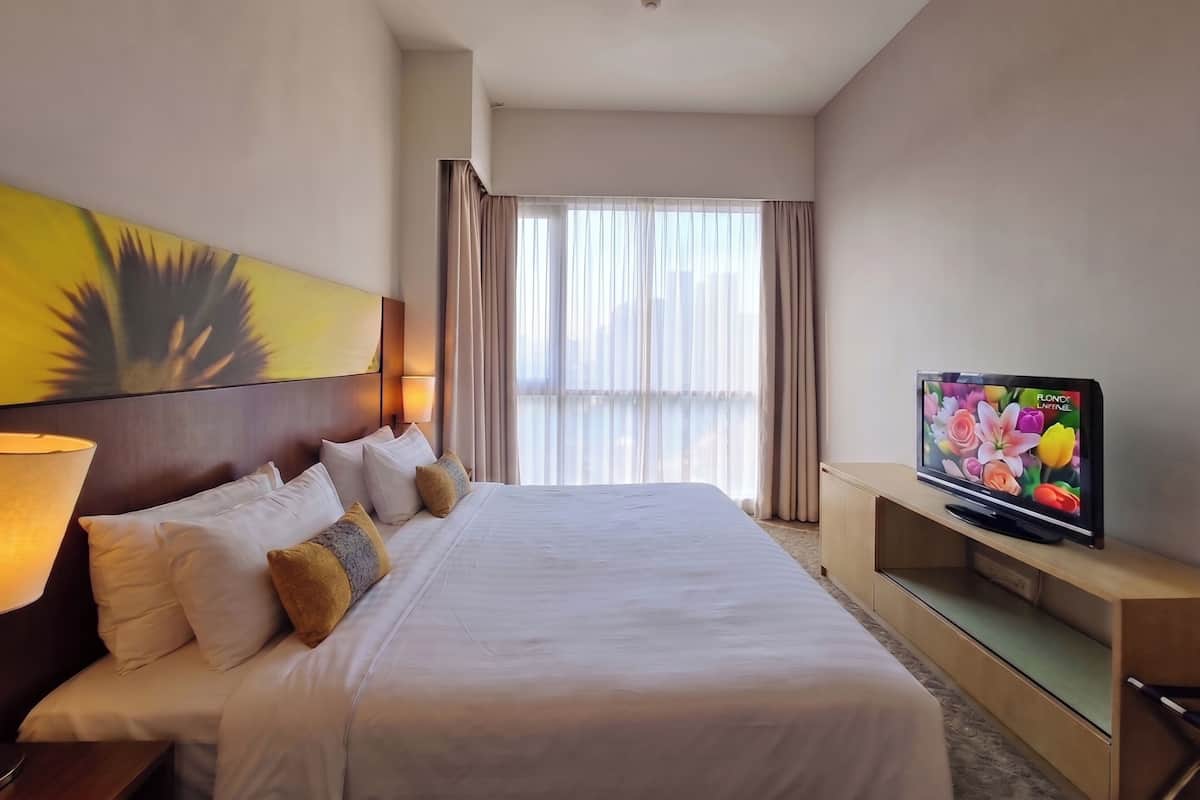 Habitació d'hotel amb un llit gran, un televisor, un quadre i una finestra amb cortines.