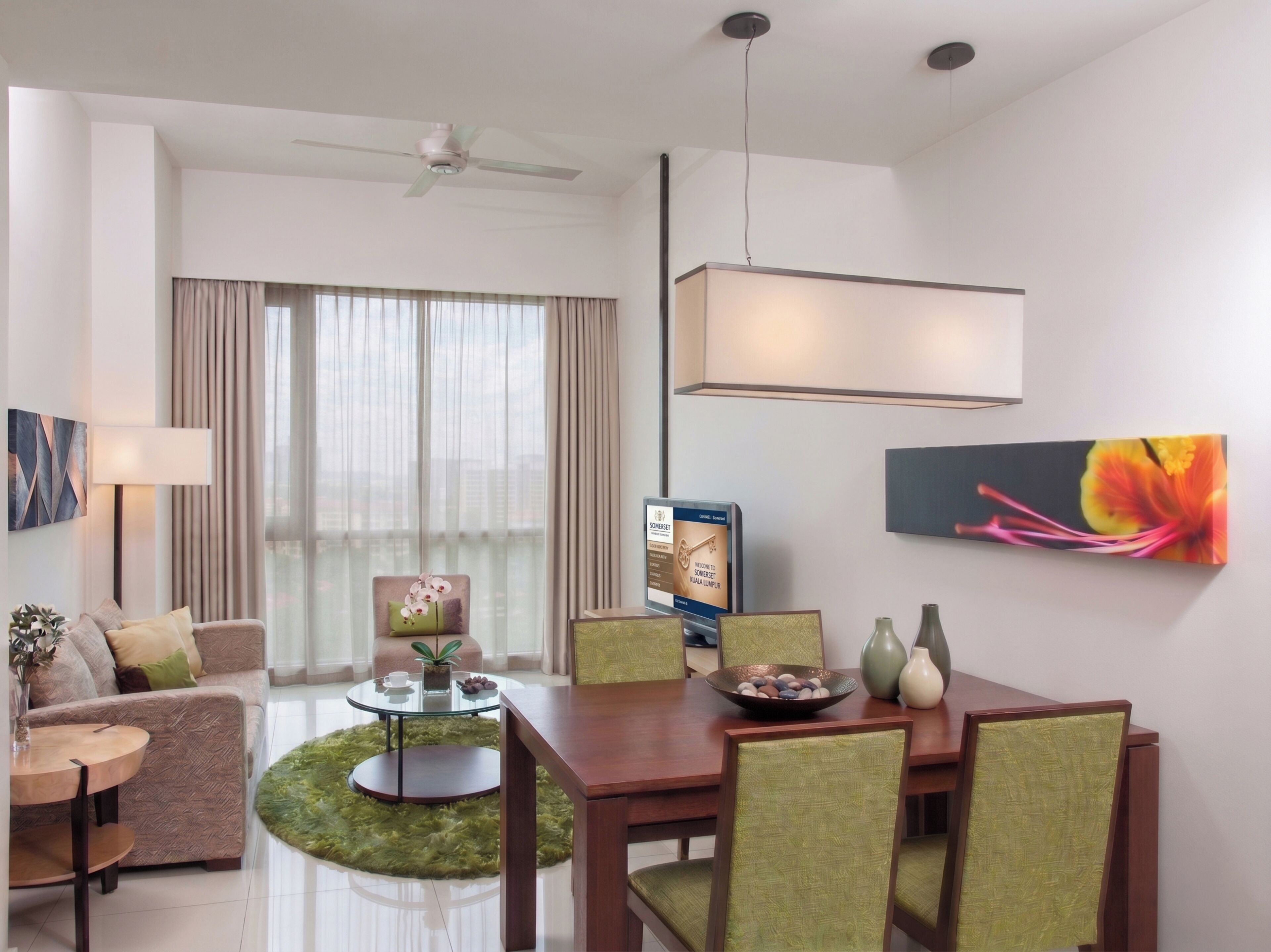 A modern hotel room with a dining area, a sofa, a coffee table, a chair, a TV, and a painting.