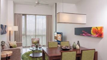 A modern hotel room with a dining area, a sofa, a coffee table, a chair, a TV, and a painting.