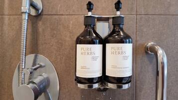 Zwei Flaschen Pure Herbs Duschgel und Conditioner-Shampoo sind an einer Wand neben einem Duschkopf angebracht.