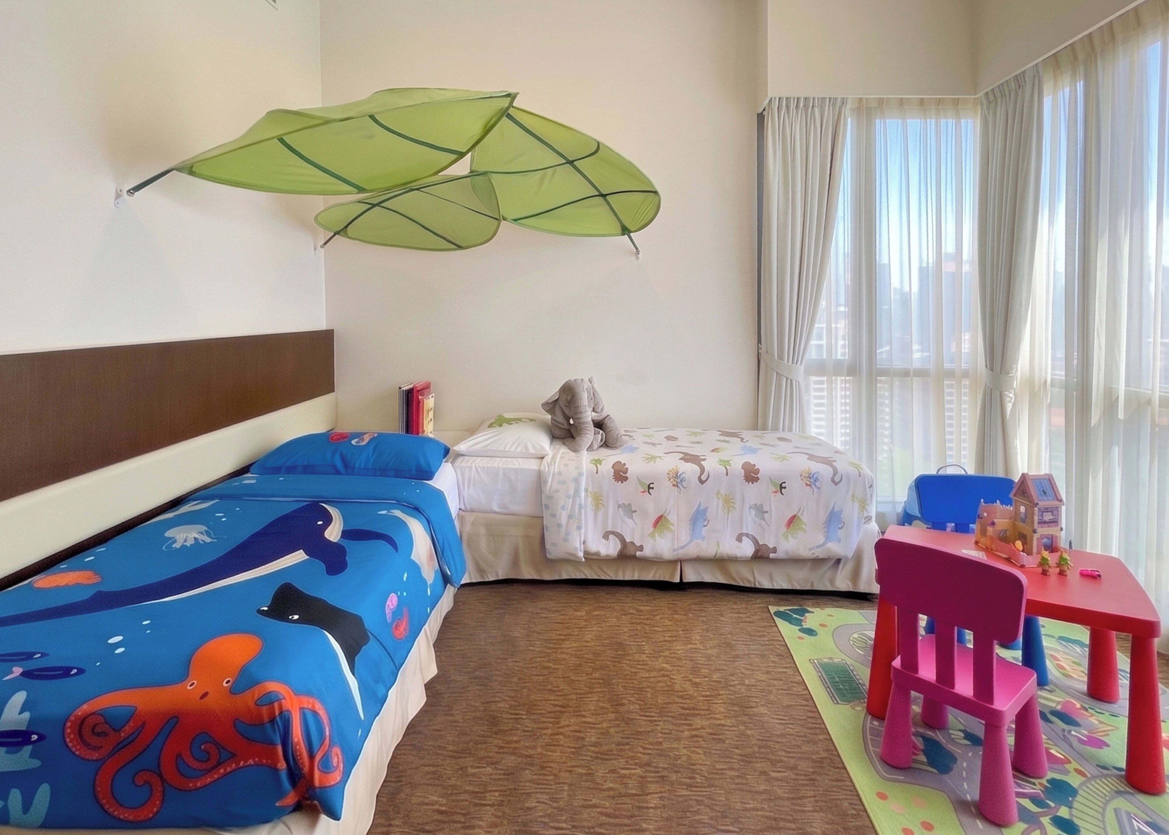 Habitación de hotel con dos camas, un escritorio con silla, una ventana con cortinas y una decoración de paraguas verdes.