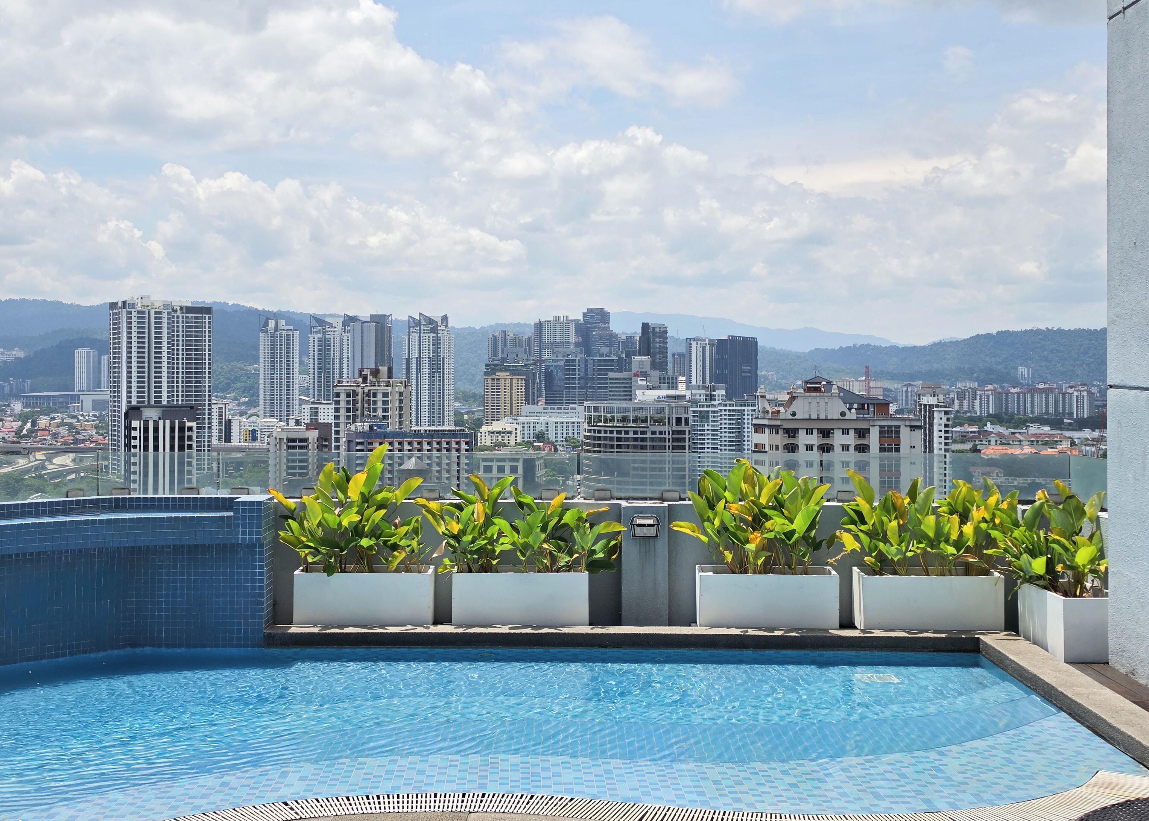 A rooftop pool with a cityscape view, potted plants, and a tiled floor.