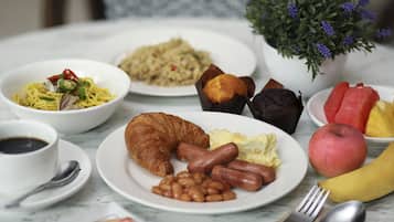 Disposição de café da manhã com pratos de comida, incluindo ovos, salsichas, feijão, croissants e frutas.