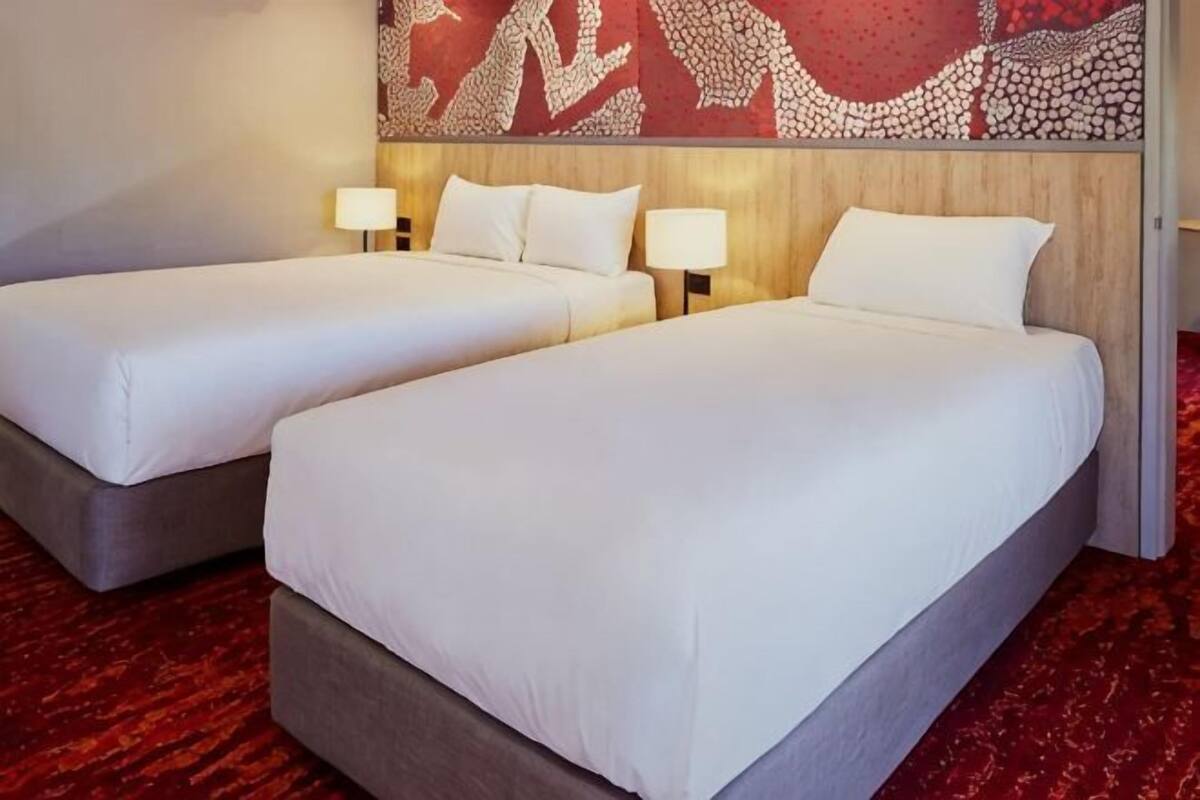A hotel room with two beds, each with a pillow and a lamp.