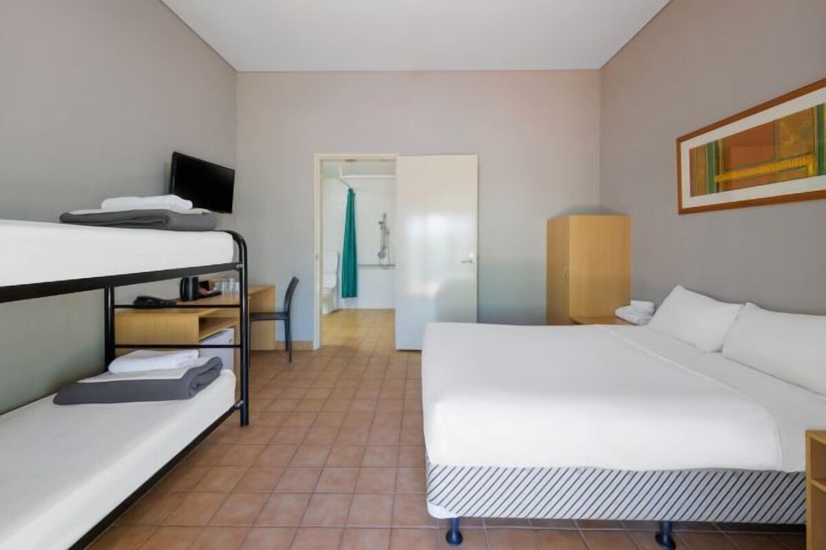 A hotel room with a bunk bed, a single bed, a television, a desk, and a wardrobe.
