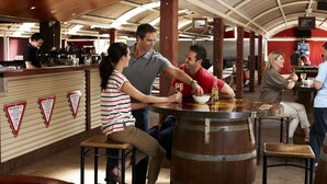 A bar area with wooden stools, a counter, and a large wooden barrel. - The Outback Hotel (Yulara)