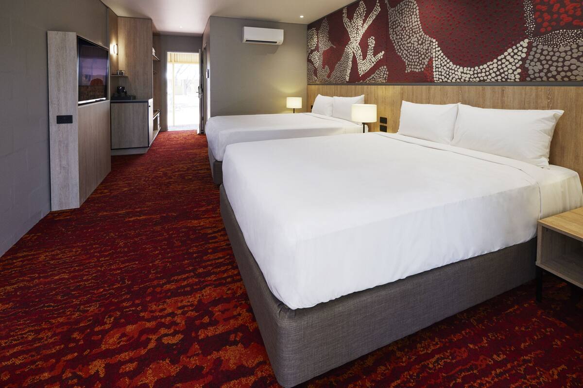 A hotel room with two beds, a kitchenette, and a red carpeted floor.
