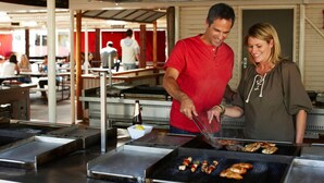 A man and a woman grilling food at an outdoor restaurant with multiple grilling stations and tables. - The Outback Hotel (Yulara)