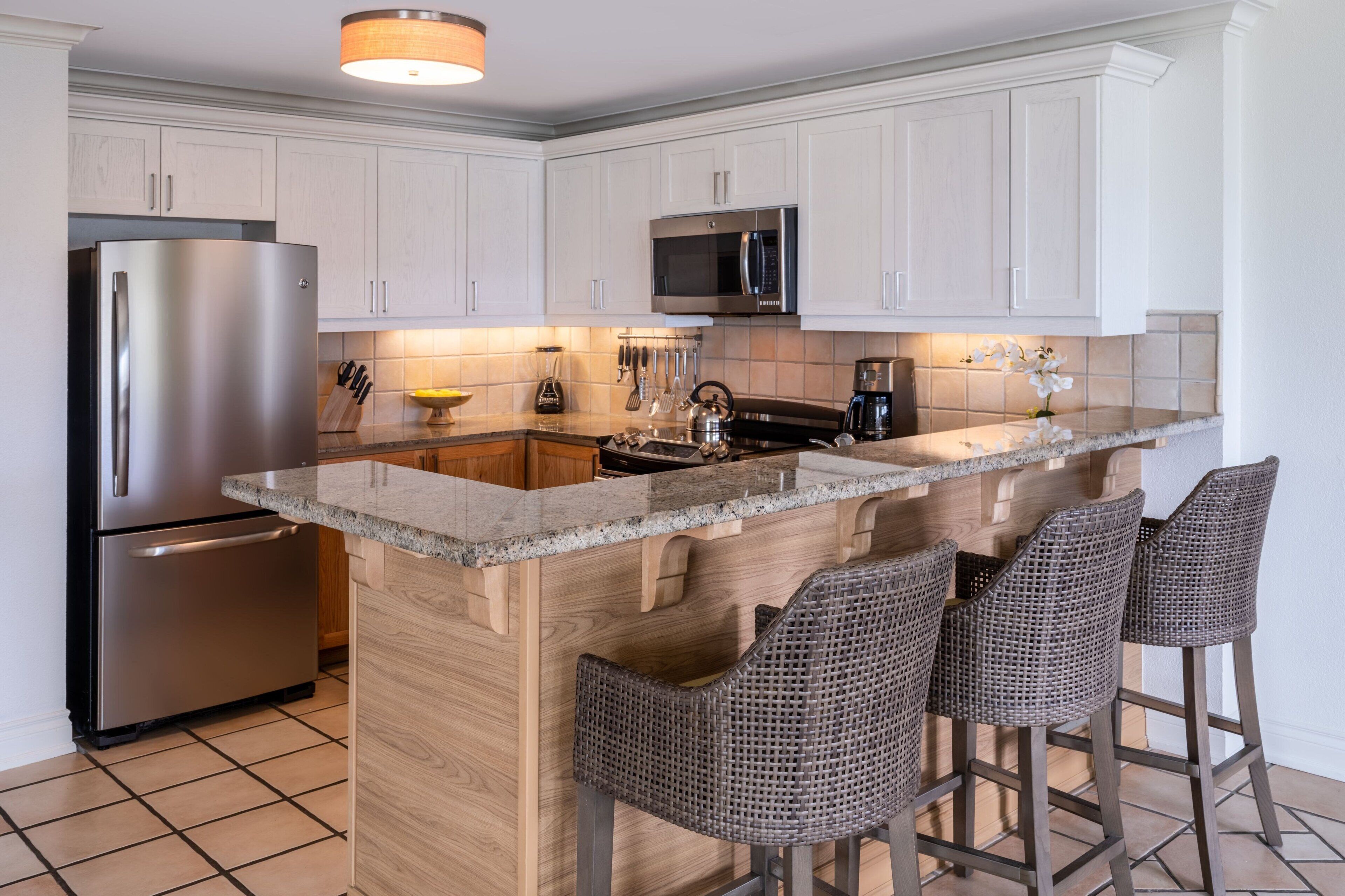 Una cocina moderna con armarios blancos, electrodomésticos de acero inoxidable y una isla central con taburetes de bar.