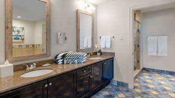 A bathroom with a double sink vanity, a large mirror, and a shower area.