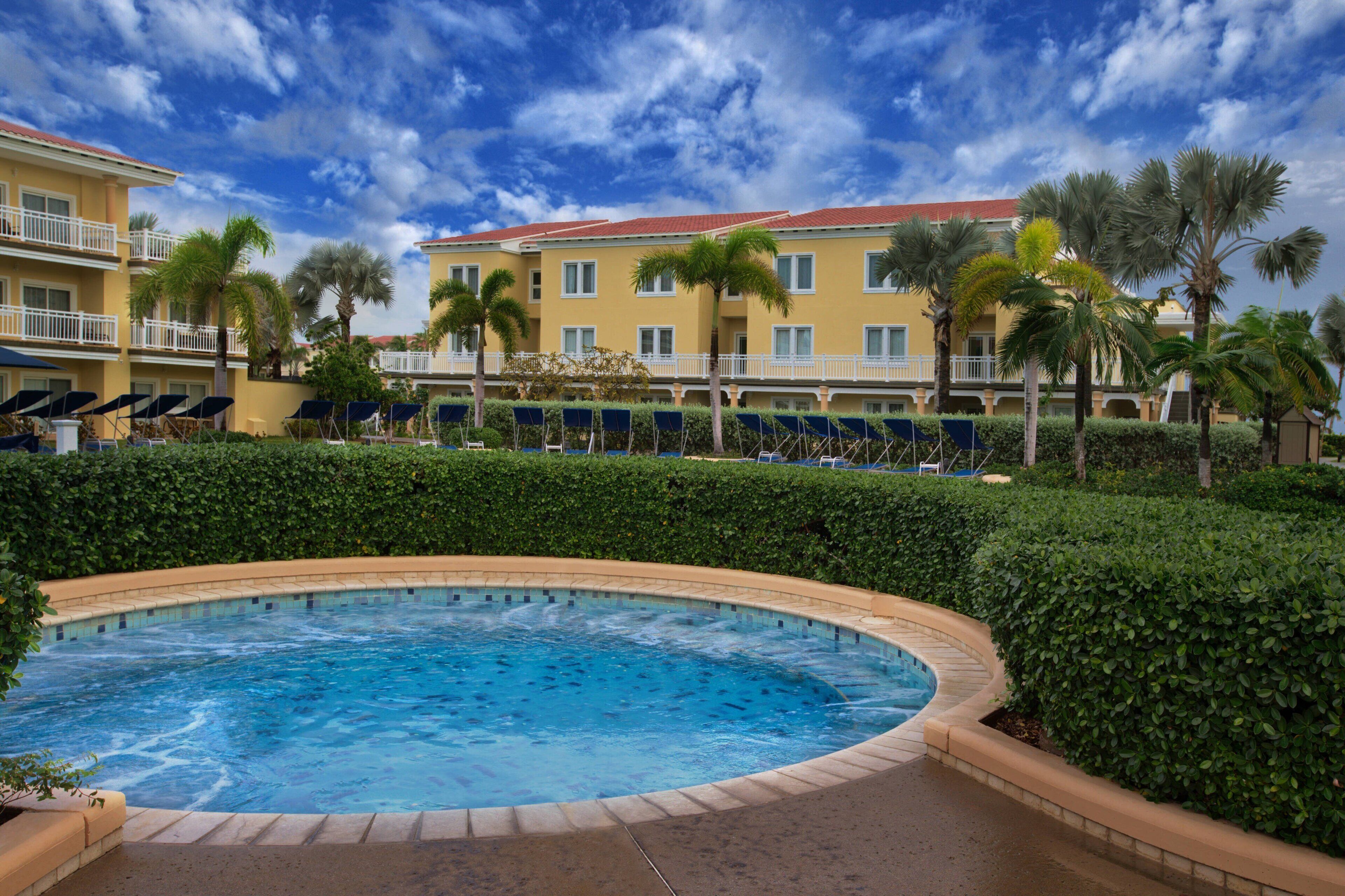 Ein Hotel mit Pool, umgeben von Palmen und wolkenlosem, blauem Himmel.