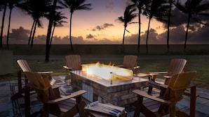 An outdoor seating area with a fire pit surrounded by wooden chairs, overlooking a beach with palm trees and a sunset. - Marriott's St. Kitts Beach Club (Basseterre)