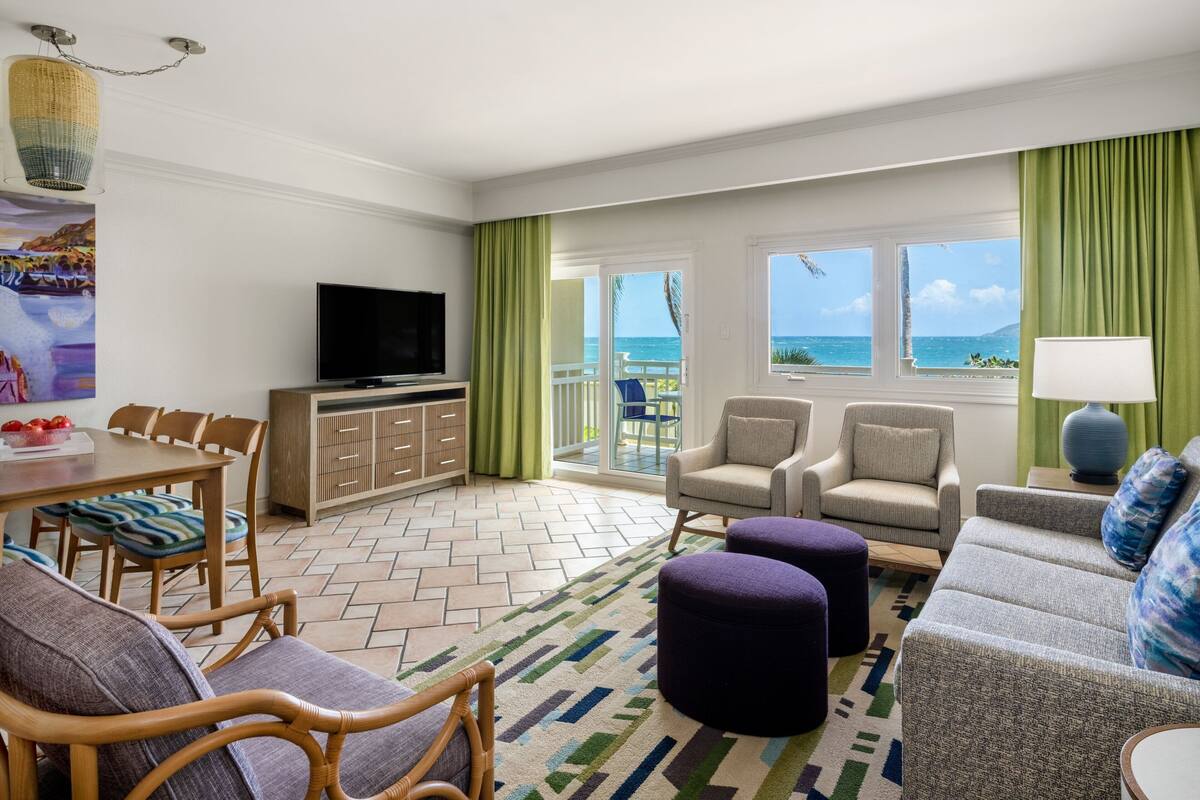 A hotel room with a balcony, a dining area, a sofa, and a television.