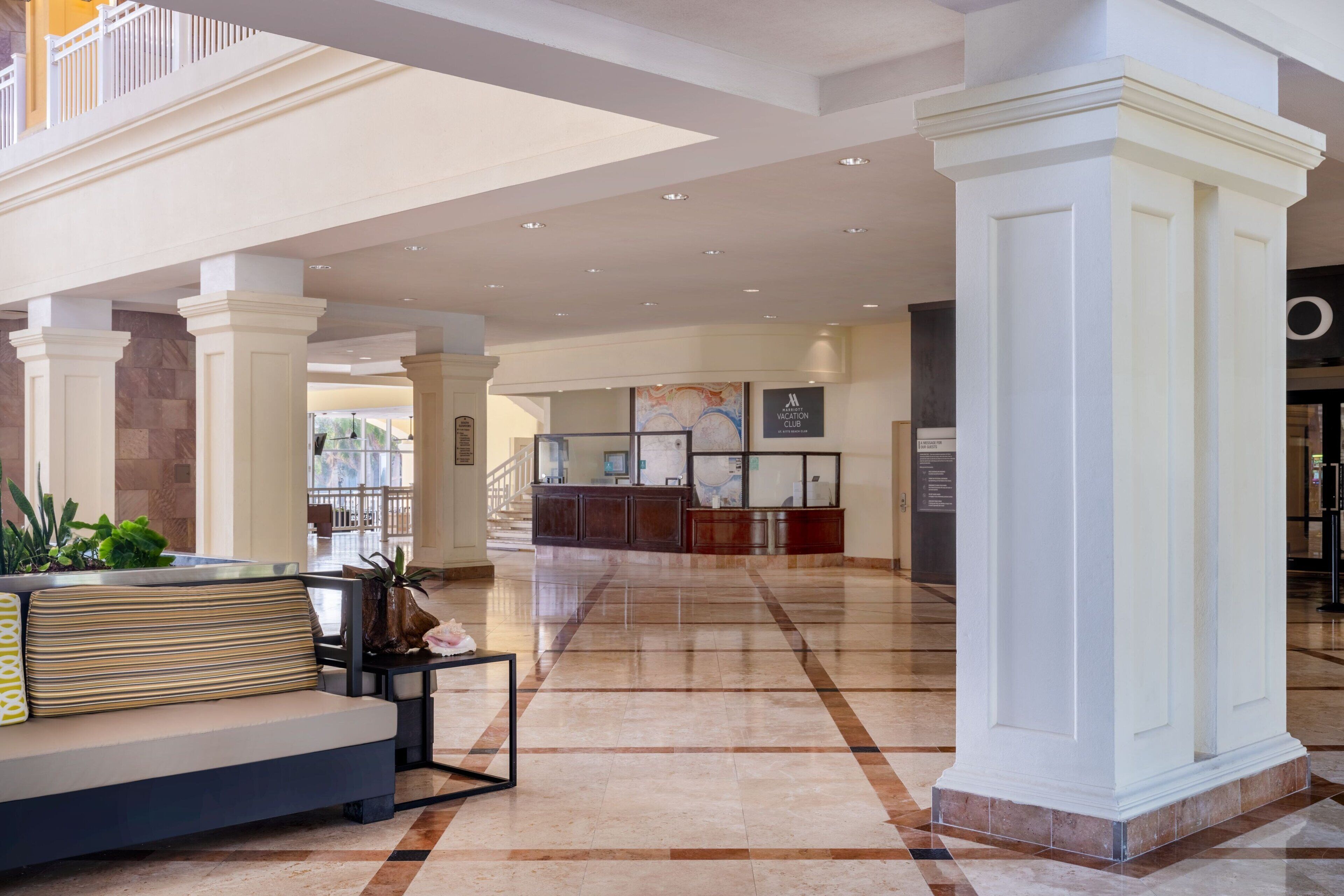 Un vestíbulo amplio con mostrador de recepción, zona de estar con sofá y mesa de centro, y un gran jarrón decorativo.