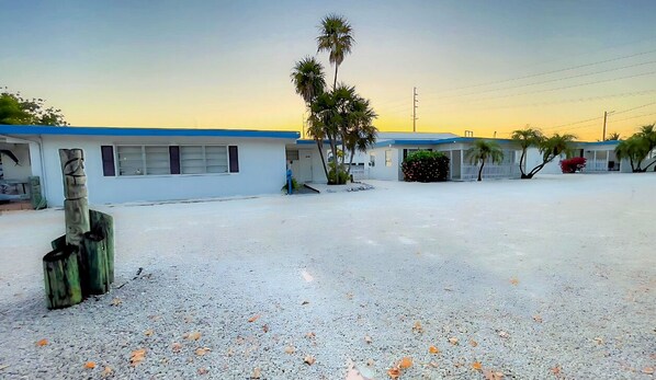 Un motel con aparcamiento de grava, palmeras y cielo despejado.