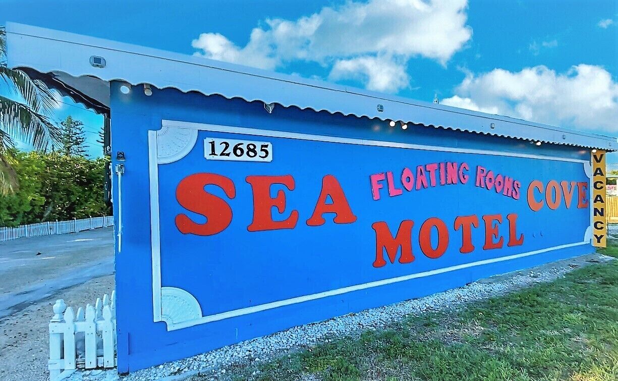 Un edificio azul con un letrero que dice "SEA FLOATING ROOMS COVE MOTEL" y el número "12685".