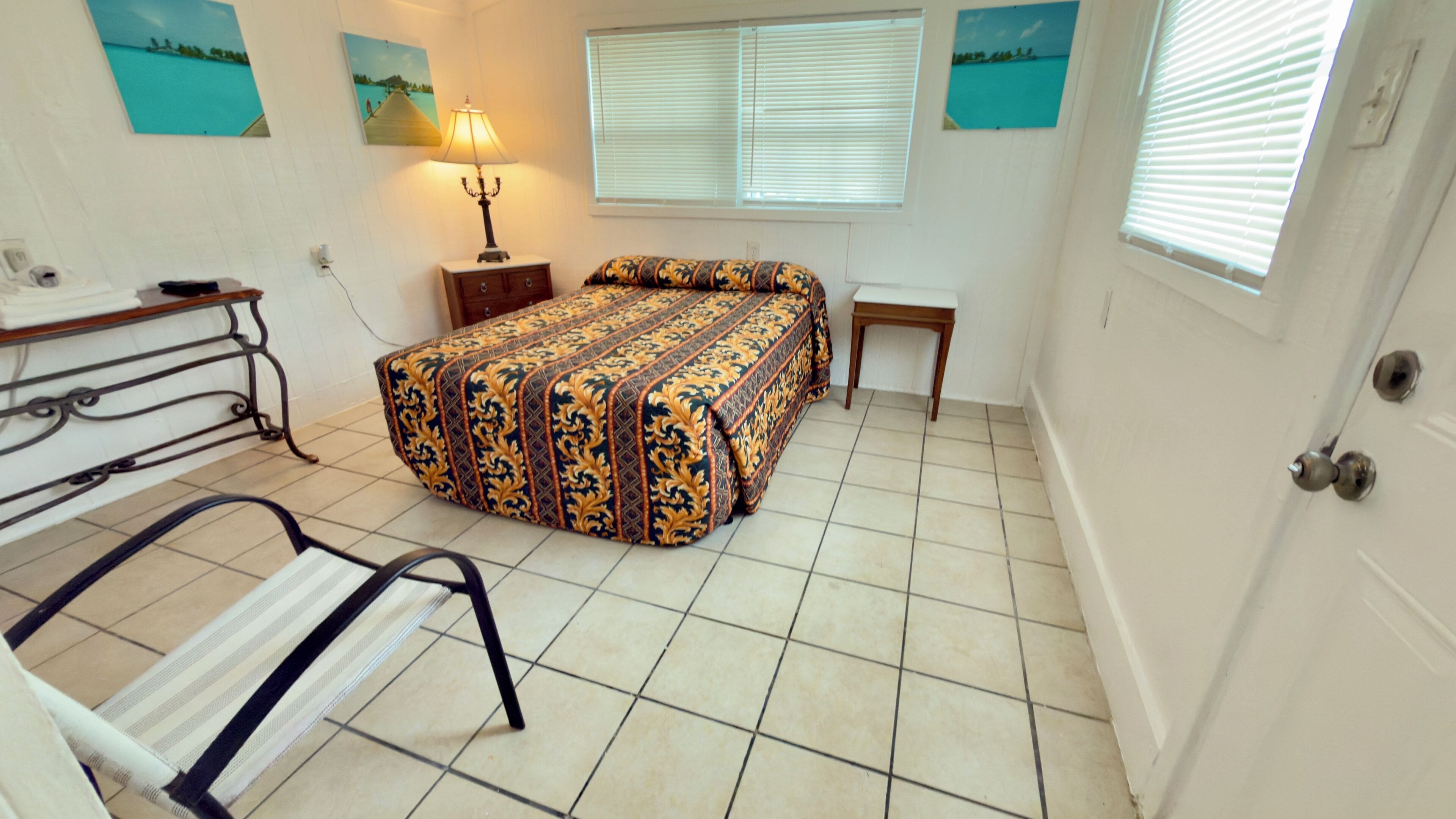 A small, neatly arranged bedroom with a bed, bedside table, lamp, and a chair.