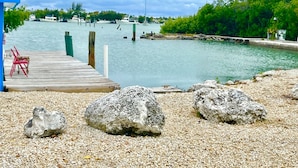 A waterfront dock with pebbles, rocks, and a red chair. - Floating Sea Cove Resort & Marina (Marathon)