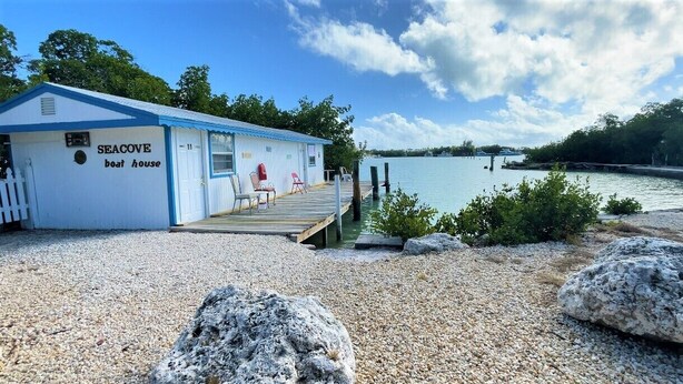 A small boat house named "SEACOVE" with a dock extending into calm water, surrounded by pebbles and rocks. - Floating Sea Cove Resort & Marina (Marathon)