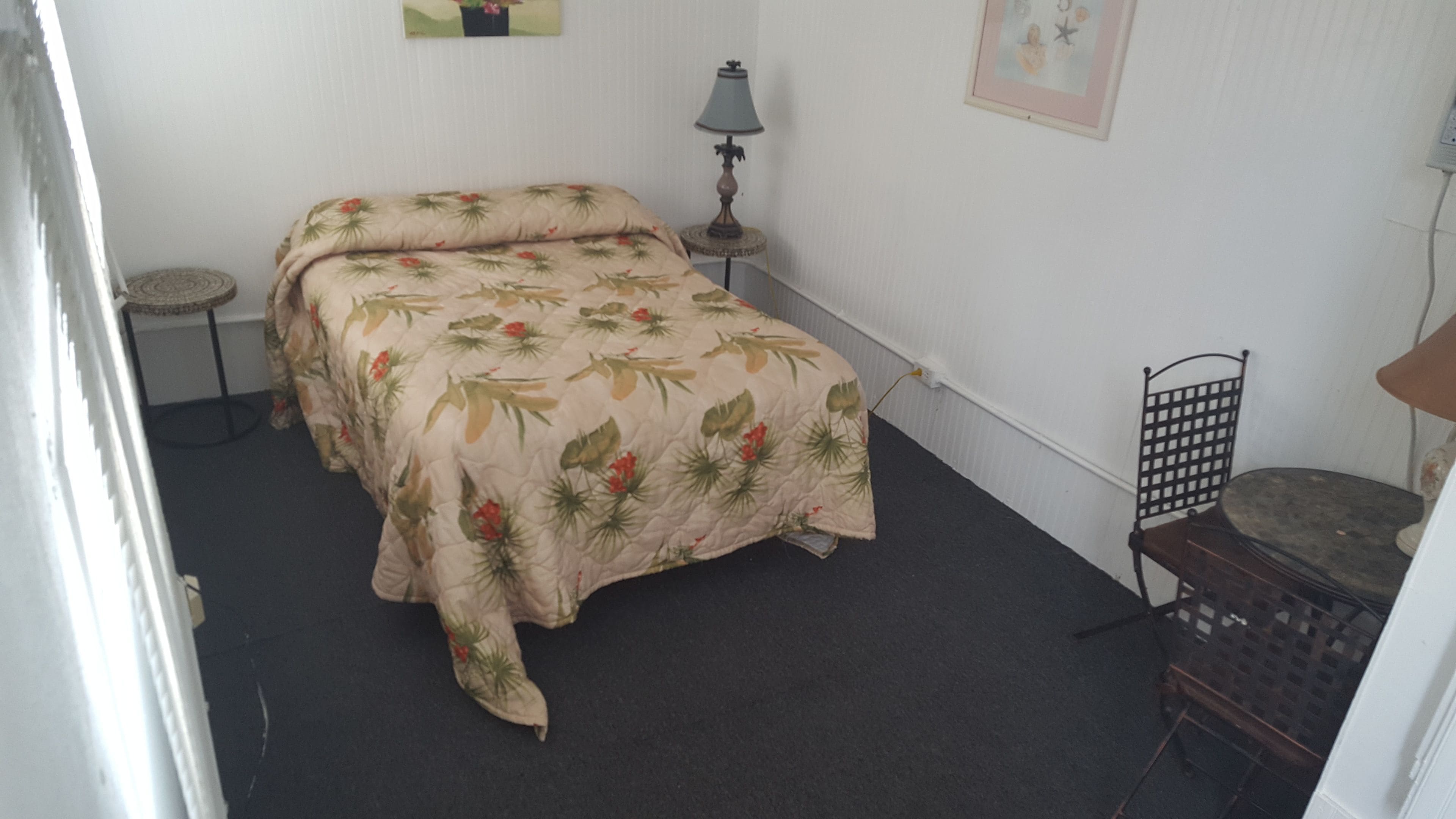 Een kamer met een bed, een klein rond tafeltje, een stoel, een lamp en een foto aan de muur.