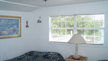 A room with a bed, a nightstand, a lamp, a window with blinds, and a painting on the wall.