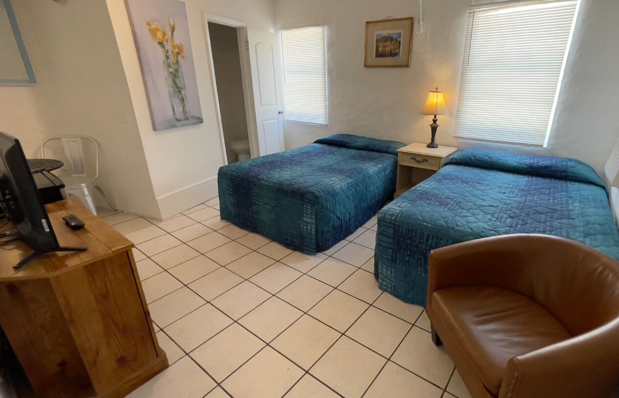 A room with two beds, a desk, a chair, and a lamp.