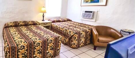A room with two beds, a chair, a desk, a lamp, and a TV.