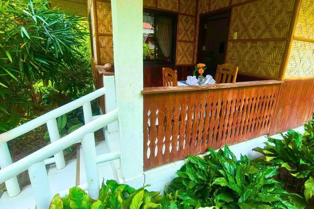 Una veranda de madera con barandilla blanca, rodeada de exuberante follaje verde.