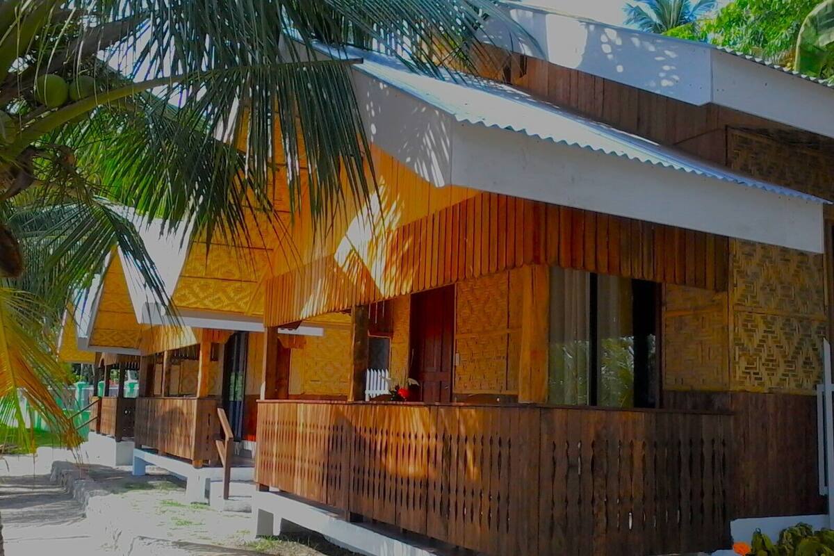 Una cabaña con fachada de madera, un balcón y vista a una palmera.